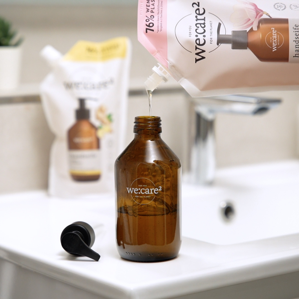 we:care² Handseife Nachfüllbeutel füllt amberfarbene Glasflasche im Badezimmer nach