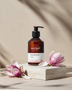Ästhetische Produktpräsentation von Handseife bei idery (we:care²): Die braune Flasche mit Magnolien-Duft steht auf einem hellen Natursteinsockel, umrahmt von zarten Magnolienblüten. Ein Spiel aus Licht und Schatten im Hintergrund unterstreicht das hochwertige, nachhaltige Design der Pflegeprodukte.